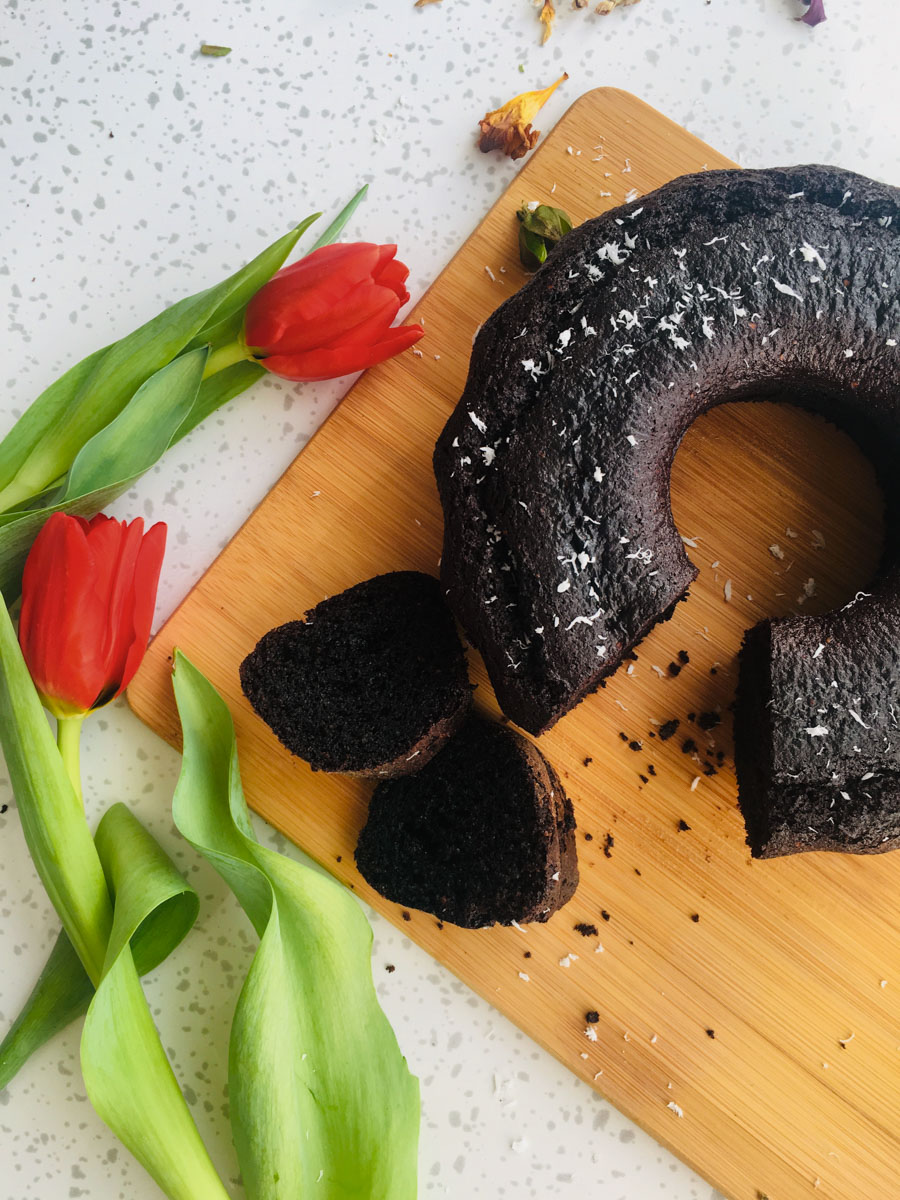 Two pieces of brownie cake and a paleo brownie cake on a wooden board. A red tulip next to them.