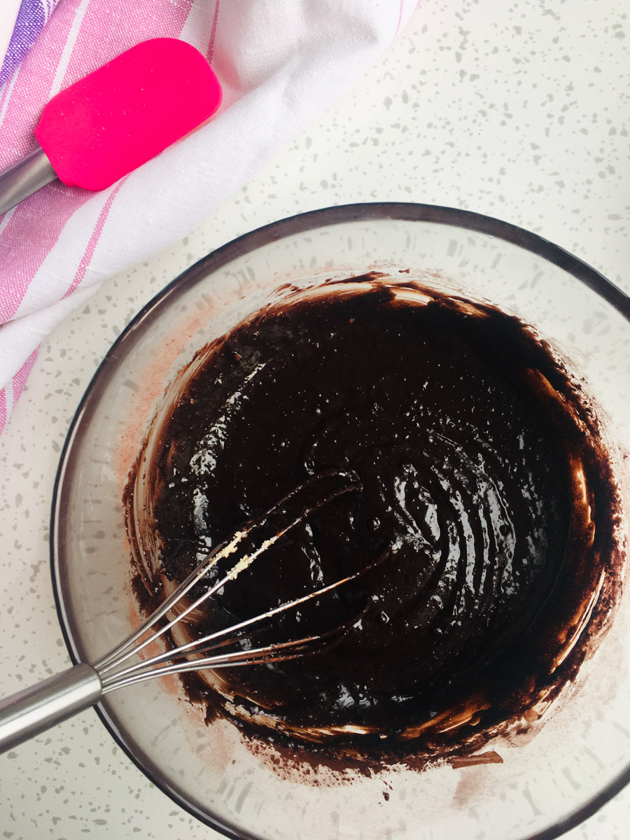 Glass bowl with mixed in cocoa powder, almond flour, baking soda. A spatula inside the bowl.