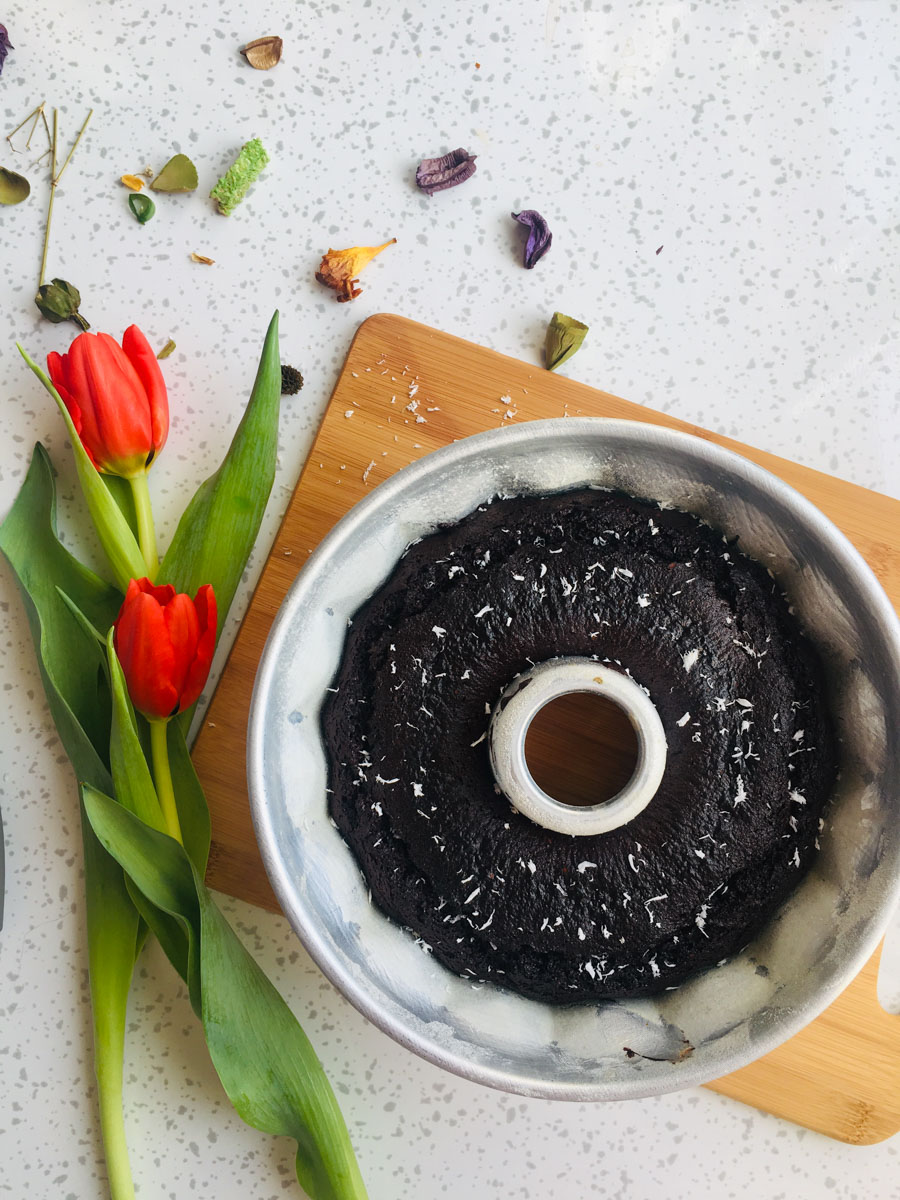 Brownie Cake with coconut flakes on top. Two red tullips on the left side of the bowl.