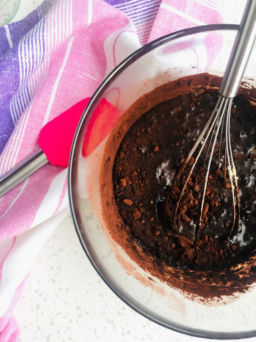 Glass bowl with cocoa mixture in it and a spatula inside the bowl. Another pink spatula next to the bowl. 