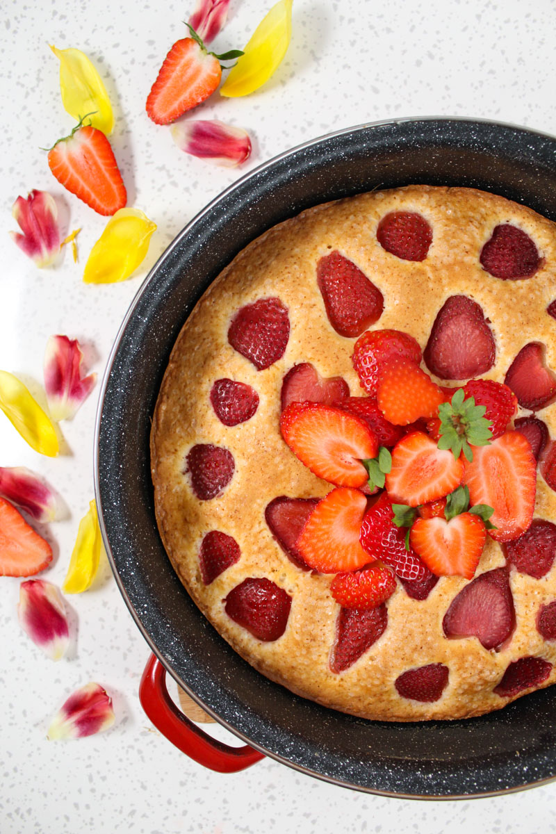 a pan with strawberry cake in it and flower petals on the left side of it