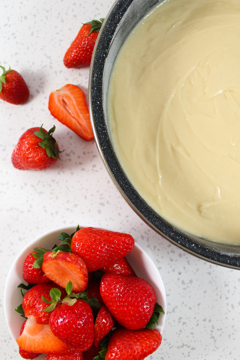 A bowl full with strawberries and a pan with cake batter