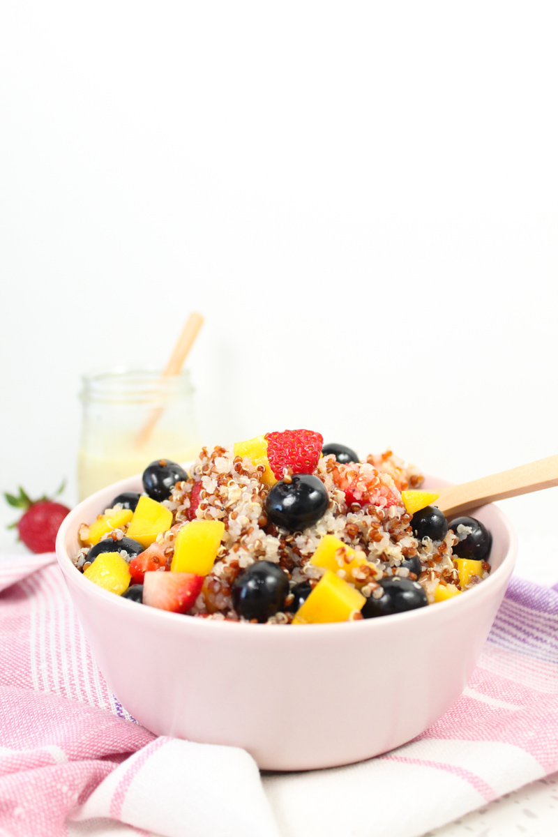 pink cup with quinoa mango and blueberry salad. Strawberries and a dressing in the background