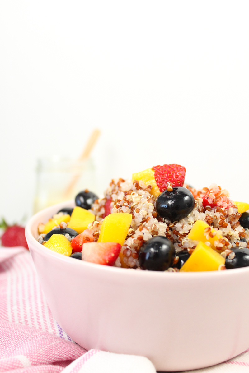 pink cup with quinoa mango and blueberry salad. Strawberries in the background from very close