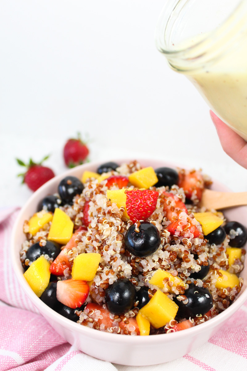 pink cup with quinoa mango and blueberry salad. Strawberries in the background from close