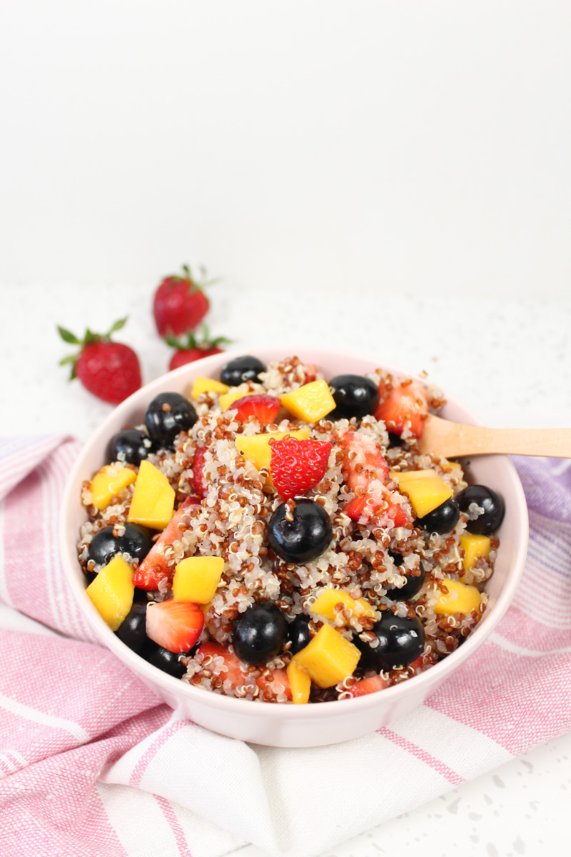 pink cup with quinoa mango and blueberry salad. Strawberries in the background 