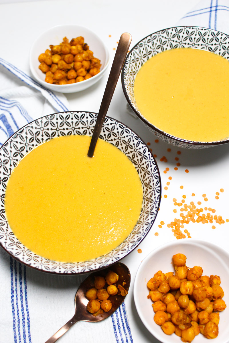 Bowls with red lentil soup and smaller bowls with chickpeas on the side